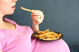 Eine Person in einem rosa Hemd, die einen Teller mit Pommes frites in der Hand hält und einen sichtbaren Schwangerschaftsbauch hat.