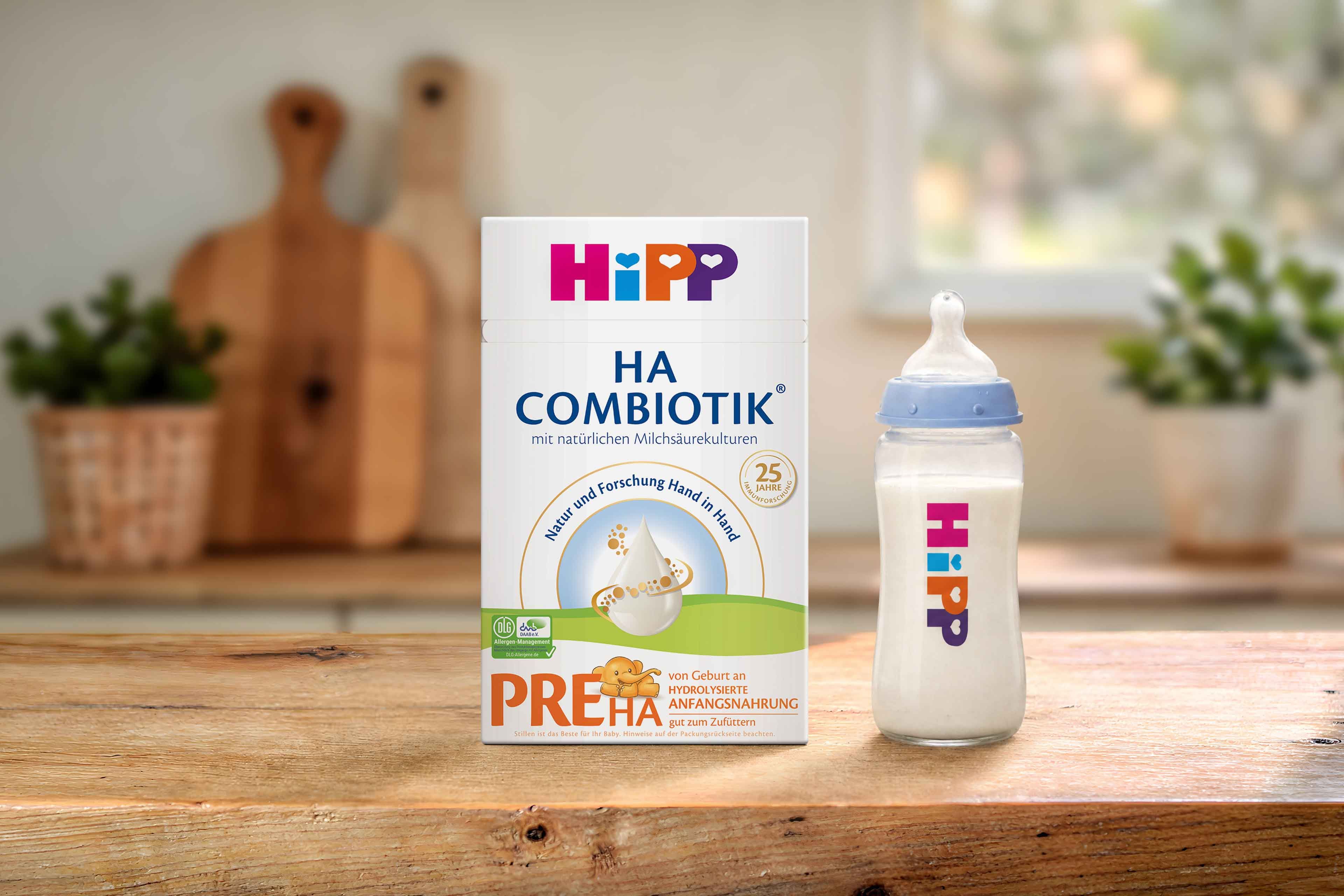 HiPP PRE HA COMBIOTIK® Anfangsnahrungspackung neben gefülltem Babyfläschchen auf Holztisch in heller Küche