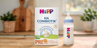 HiPP PRE HA COMBIOTIK® Anfangsnahrungspackung neben gefülltem Babyfläschchen auf Holztisch in heller Küche