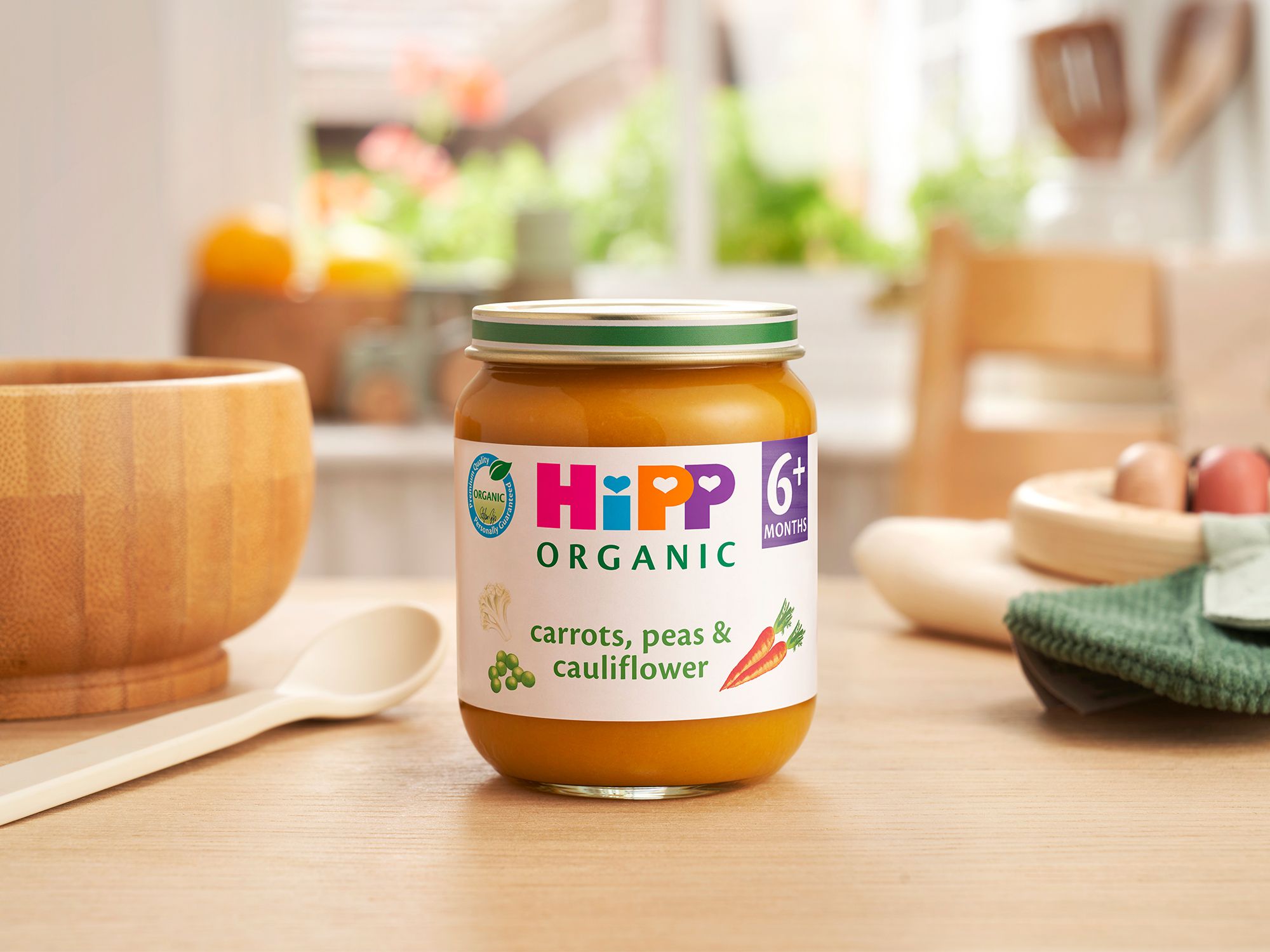 HiPP Organic Carrots, Peas & Cauliflower jar on a dining table next to a bowl and spoon