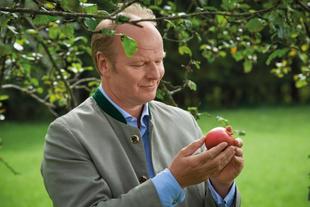 Stefan HiPP hält einen Apfel in der Hand unter dem Apfelbaum