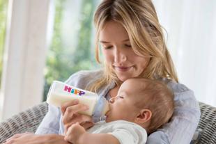 Frau sitzt in einem Sessel und füttert ein Baby mit einer Flasche