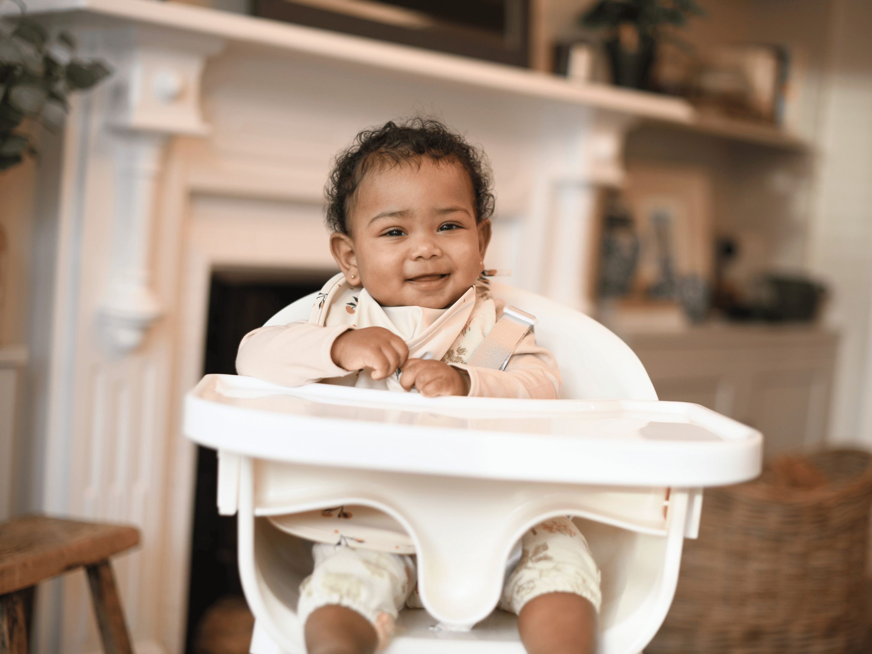 Smiling baby sitting in a high chair at home, ready to explore new weaning flavours