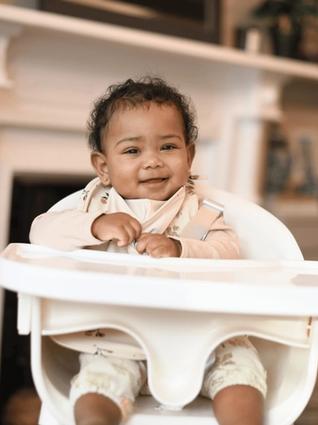 Smiling baby sitting in a high chair at home, ready to explore new weaning flavours