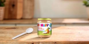 HiPP Bio Babygläschen Williams-Christ-Birne ab 5. Monat mit Löffel auf Holztisch in heller Küche