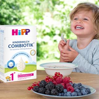 Lachendes Kleinkind frühstückt mit HiPP Kindermilch COMBIOTIK®, Beerenobst und Getreidebrei für eine ausgewogene Nährstoffversorgung.