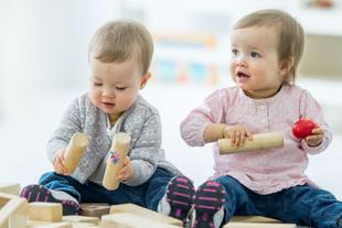 Zwei Babys sitzen auf dem Boden und spielen mit Bauklötzen.