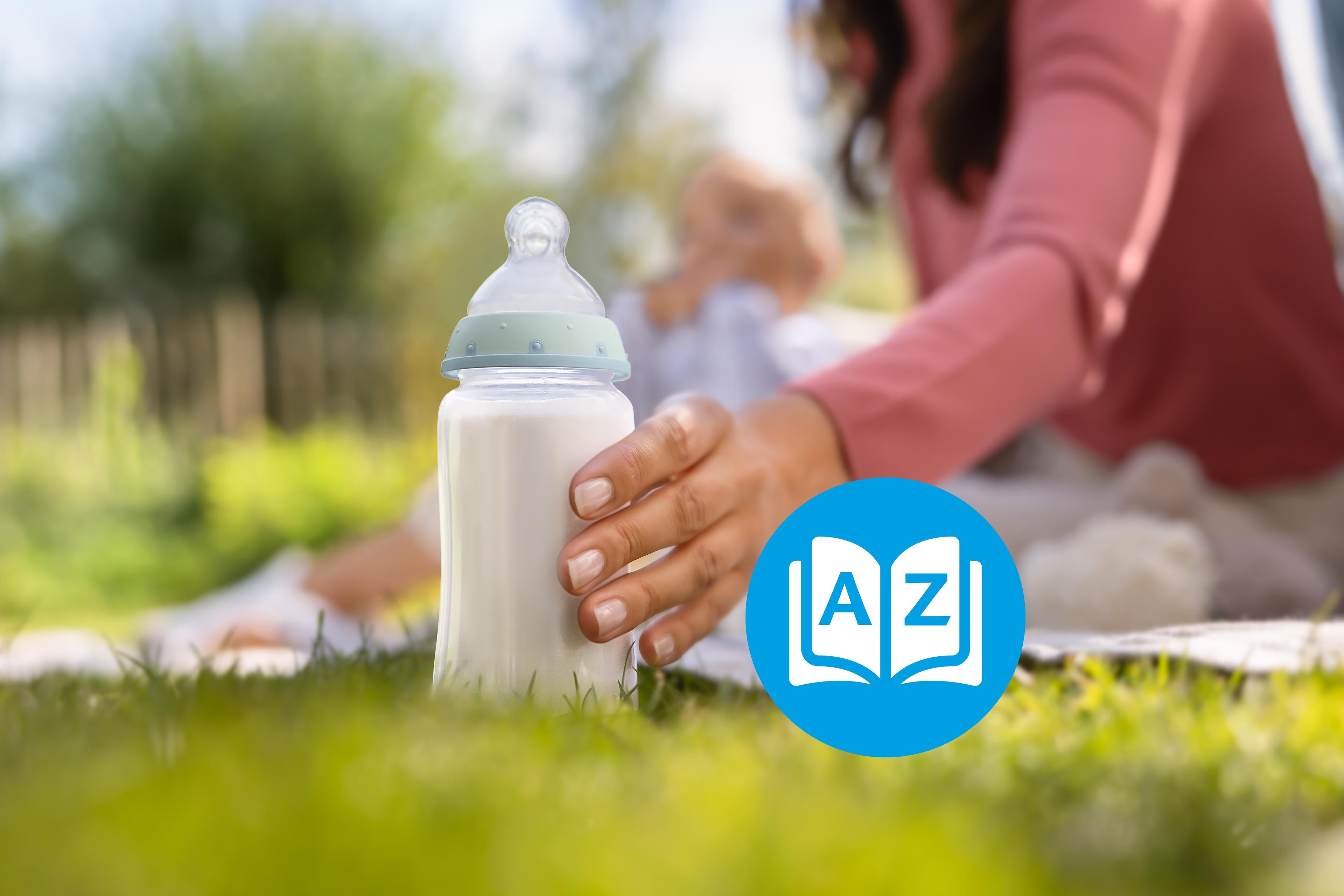 Elternhand greift im Grünen nach einer Babyflasche mit Milch, im Hintergrund liegt ein entspanntes Baby auf der Decke.