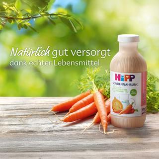 Frische Bundmöhren auf Holztisch vor grünem Hintergrund mit dem Schriftzug „Die natürlichste Art der künstlichen Ernährung“.