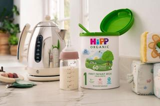 HiPP Organic first infant milk powder tin open showing the scoop, next to a kettle and bottle of milk