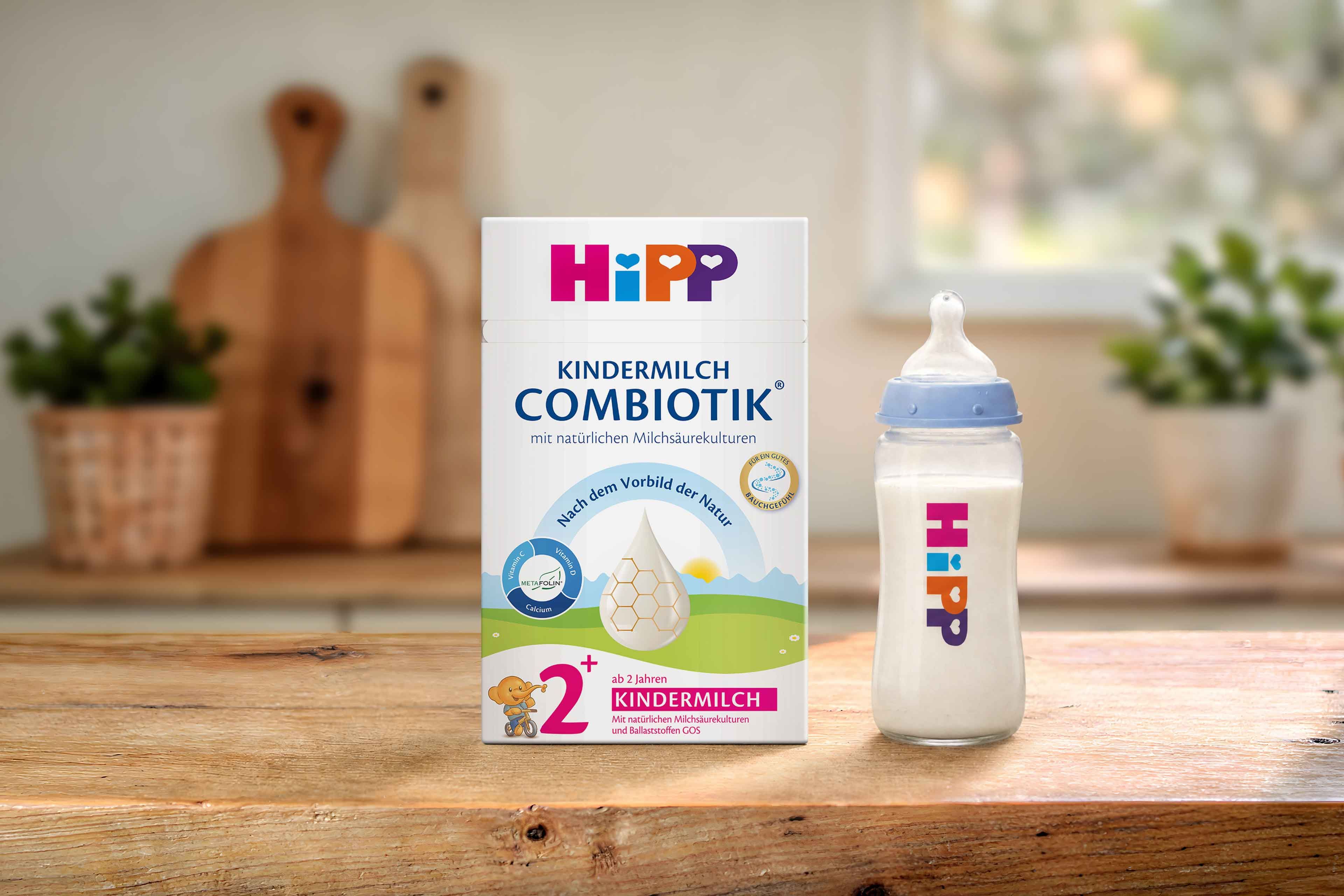 HiPP Kindermilch Combiotik 2+ Packung mit gefüllter Babyflasche auf Holztisch in heller, gemütlicher Küchenumgebung