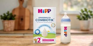 HiPP Kindermilch Combiotik 2+ Packung mit gefüllter Babyflasche auf Holztisch in heller, gemütlicher Küchenumgebung