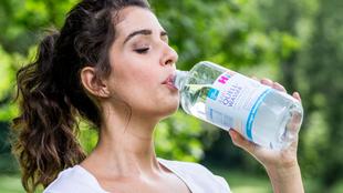 Eine Frau trinkt Wasser aus einer Flasche mit der Aufschrift "QUELLWASSER".