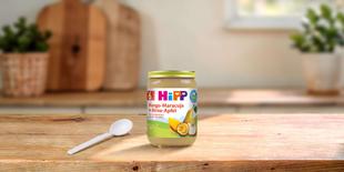 HiPP Bio Fruchtpüree Mango-Maracuja in Birne-Apfel im Glas auf Holztisch mit Löffel in heller Küche
