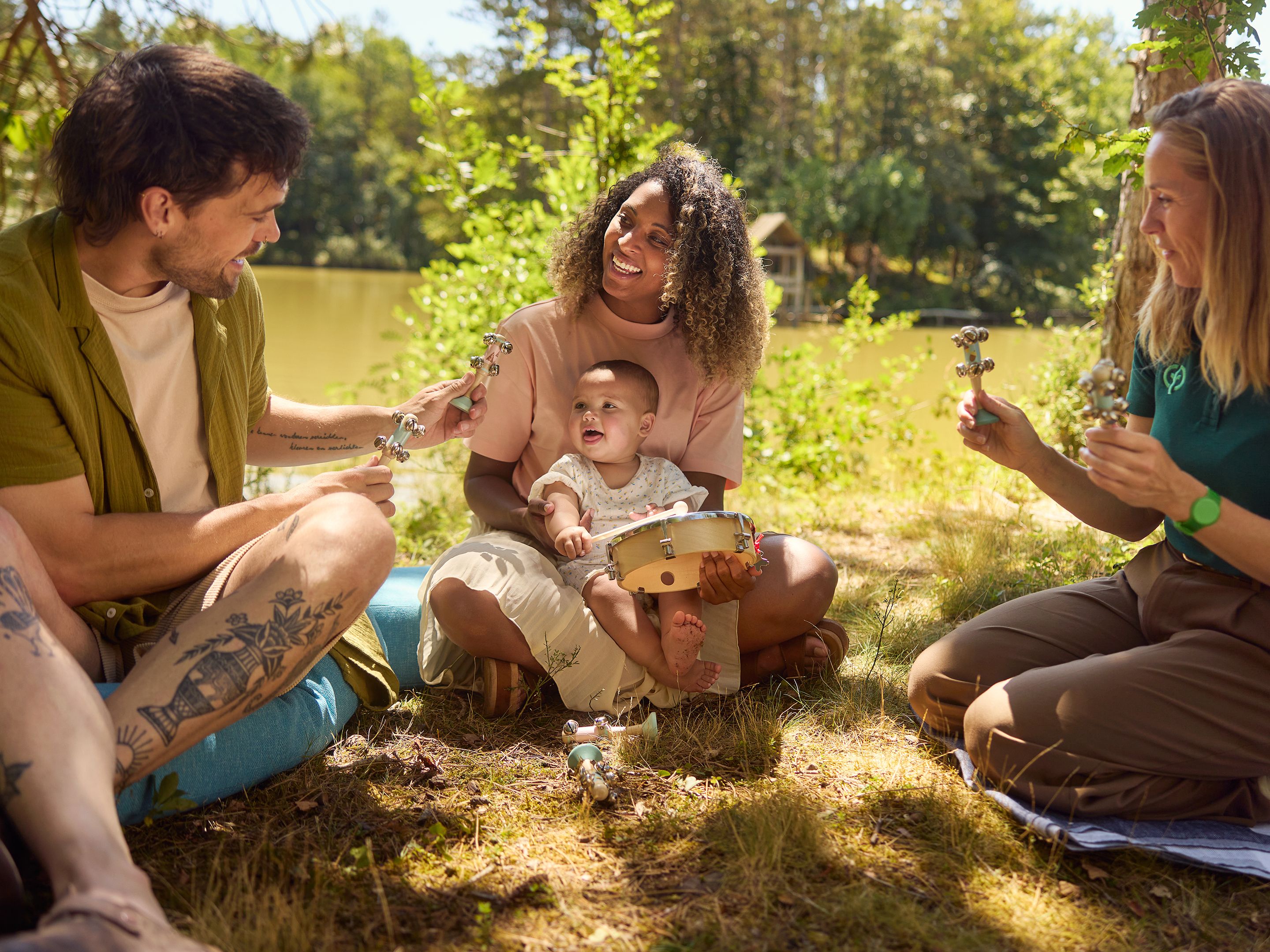 Familie sitzt mit kleinem Baby im Gras am Wasser