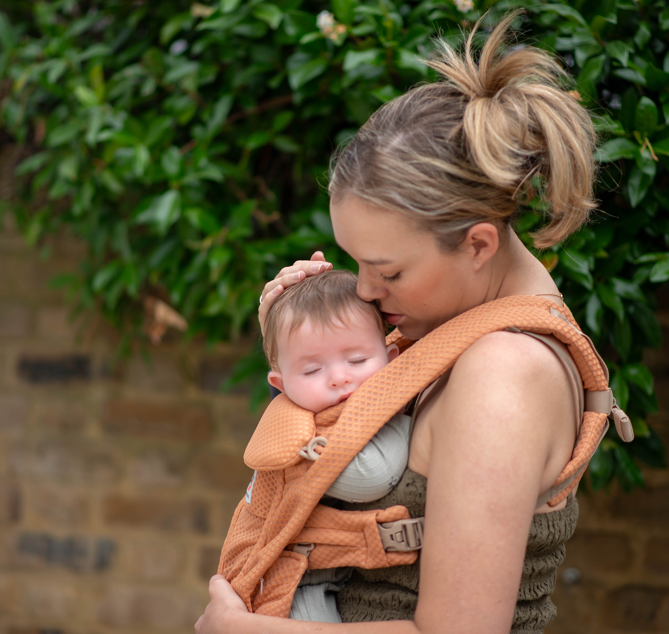 Parent cuddling a sleeping baby in a carrier outdoors, supporting calm contact napping and a soothing daytime sleep routine