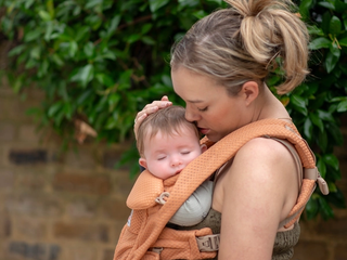 Parent cuddling a sleeping baby in a carrier outdoors, supporting calm contact napping and a soothing daytime sleep routine