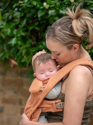Parent cuddling a sleeping baby in a carrier outdoors, supporting calm contact napping and a soothing daytime sleep routine