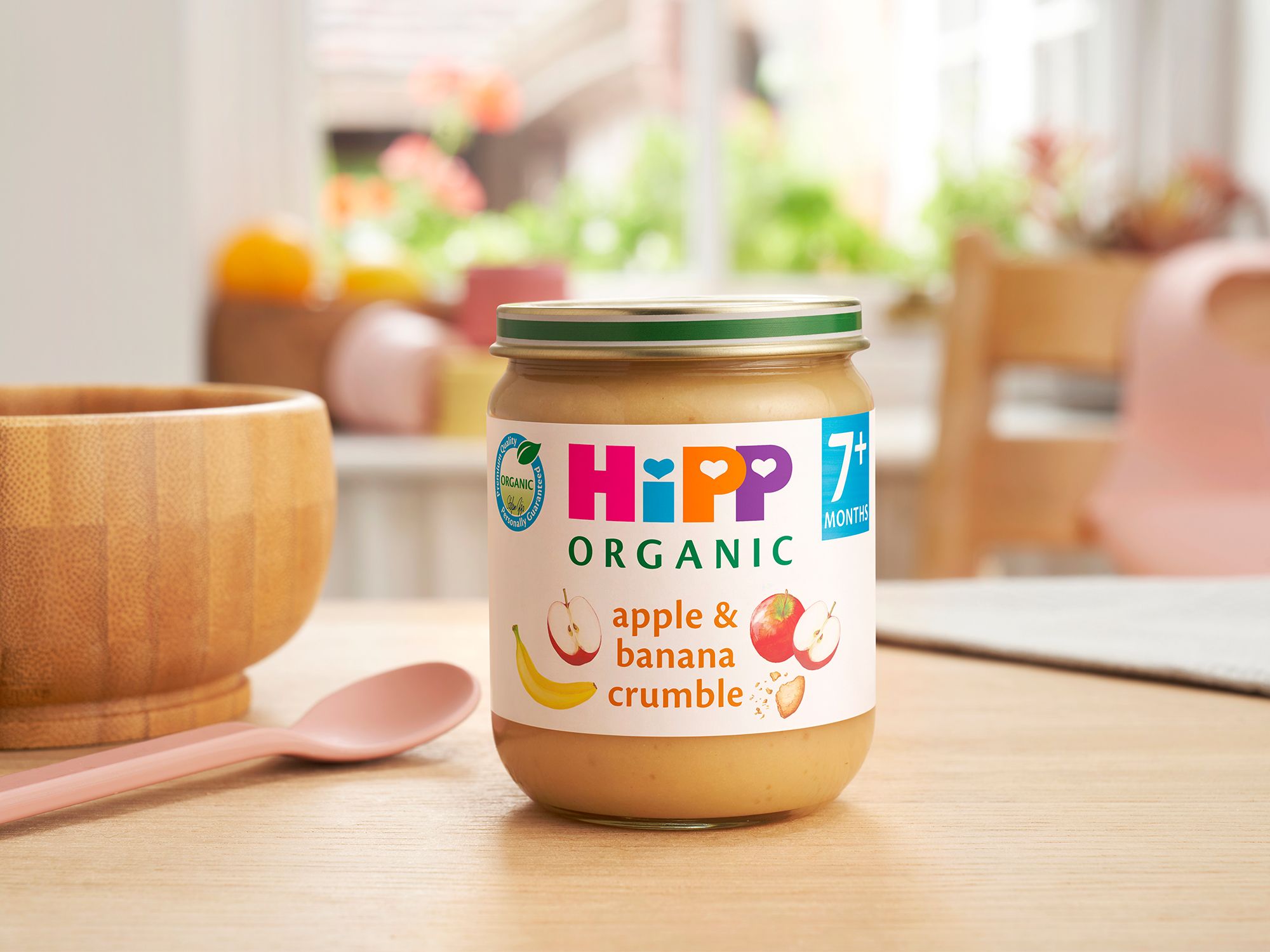 HiPP Organic Apple & Banana Crumble Jar on a dining table next to a bowl and spoon