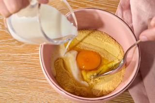 Schüssel mit Eigelb und Mehl, in die Milch gegossen wird