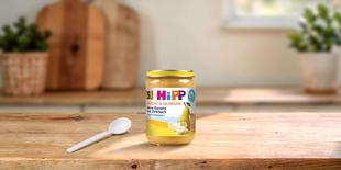 HiPP Bio-Gläschen Birne-Banane mit Zwieback, Frucht & Getreide ab 5. Monat auf Holztisch mit Löffel in heller Küche