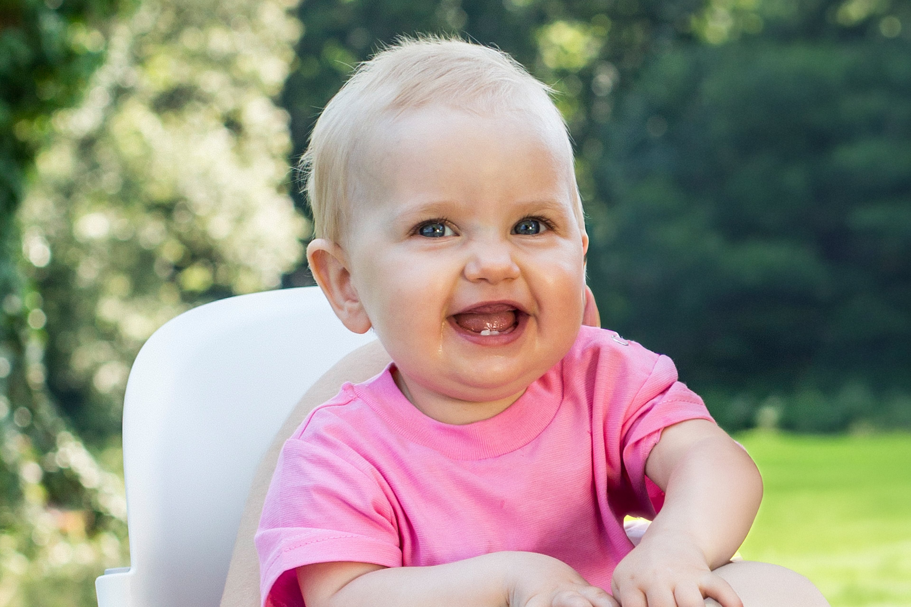 Ein Baby mit blauen Augen, das ein rosa Hemd trägt, lächelt und direkt in die Kamera schaut.