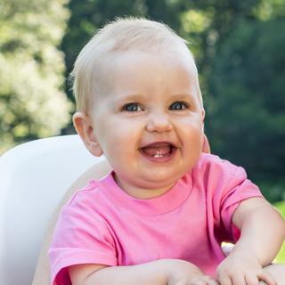 Ein Baby mit blauen Augen, das ein rosa Hemd trägt, lächelt und direkt in die Kamera schaut.