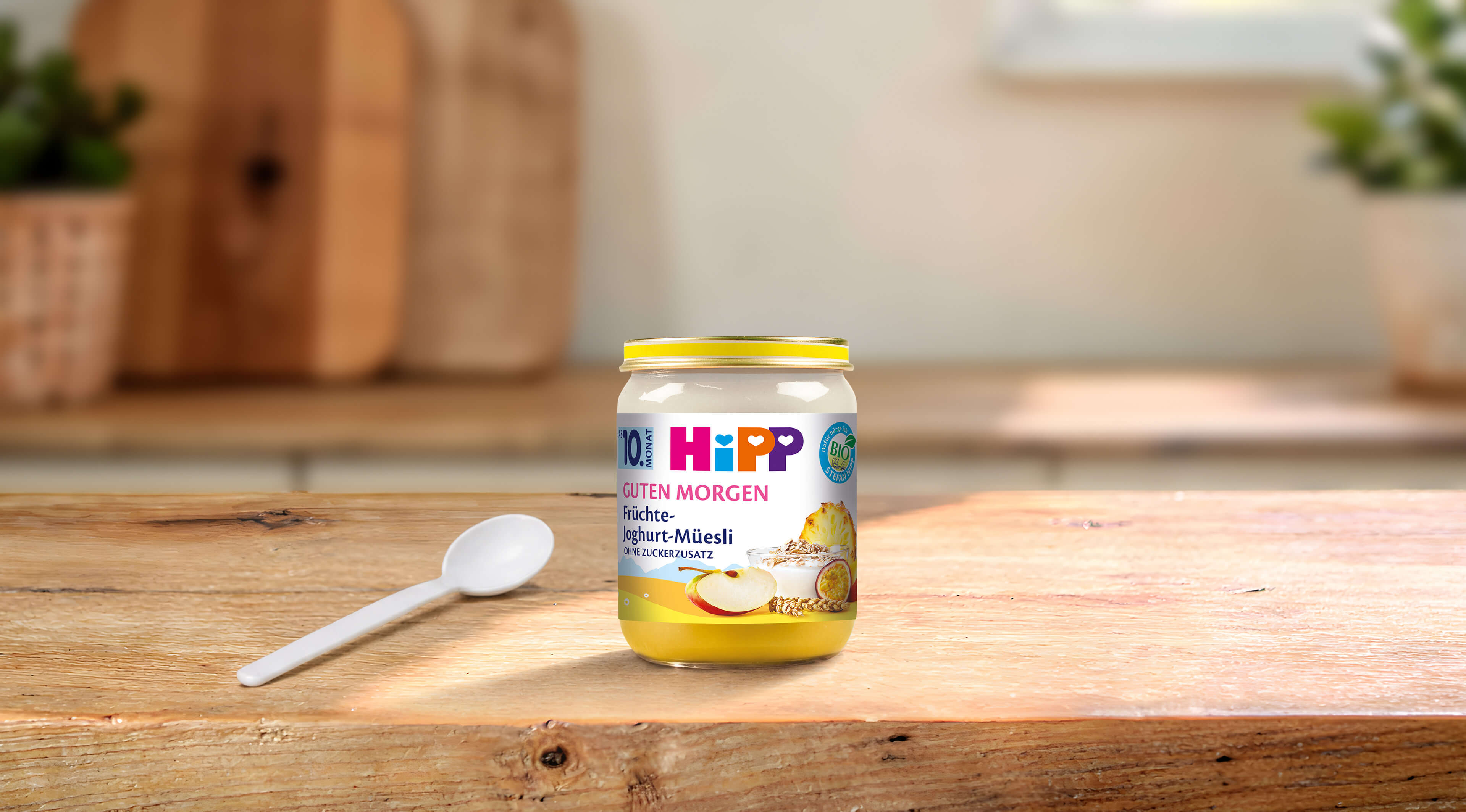 HiPP Guten Morgen Früchte-Joghurt-Müesli Bio-Gläschen mit Löffel auf einem Holztisch in heller Küche