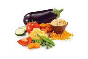 Verschiedene Gemüse- und Getreidesorten, darunter eine Aubergine, eine Tomate, Karotten, Zucchini, Erbsen, Nudeln und eine Schüssel mit roten Linsen.