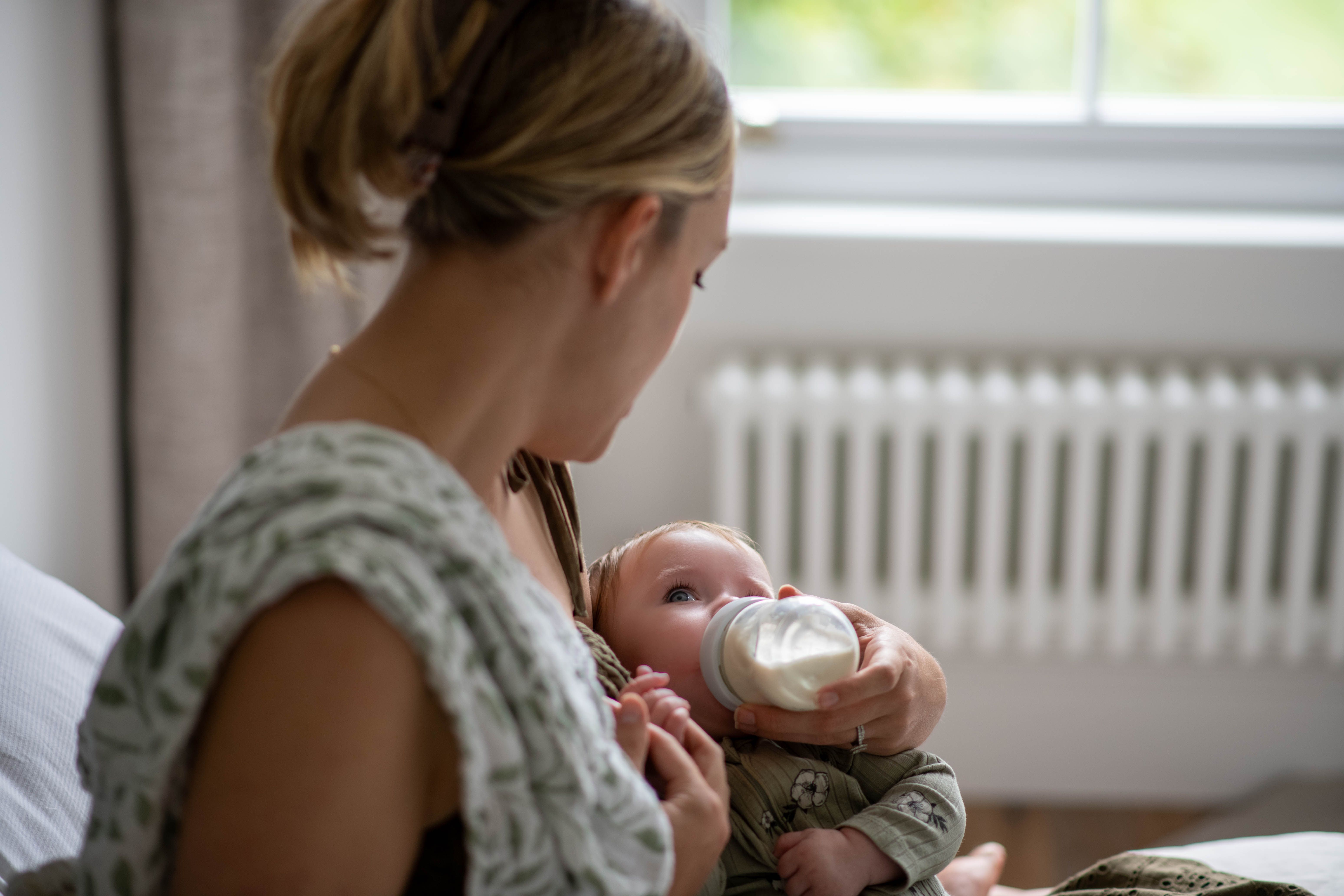 Parent gently bottle feeding a young baby, illustrating calm, nurturing combination feeding support.
