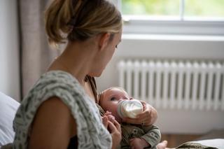 Parent gently bottle feeding a young baby, illustrating calm, nurturing combination feeding support.
