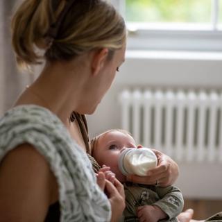 Parent gently bottle feeding a young baby, illustrating calm, nurturing combination feeding support.