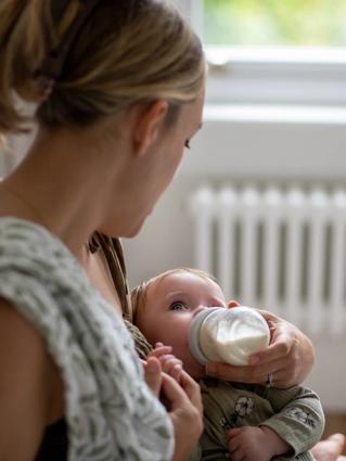 Parent gently bottle feeding a young baby, illustrating calm, nurturing combination feeding support.