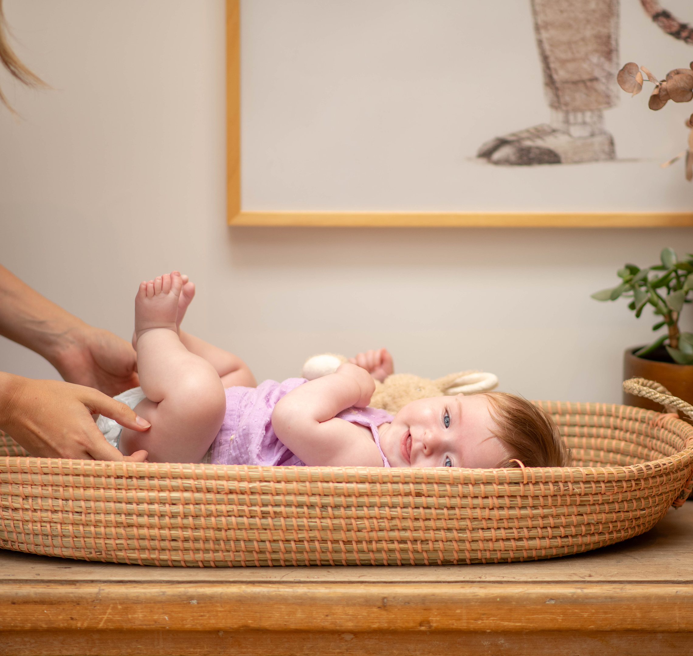 Mum changing baby in purple dress nappy, baby is smiling whilst holding her feet