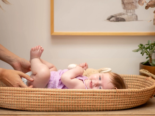 Mum changing baby in purple dress nappy, baby is smiling whilst holding her feet