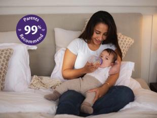 Mum sat on a bed bottle feeding her baby