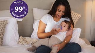 Mum sat on a bed bottle feeding her baby