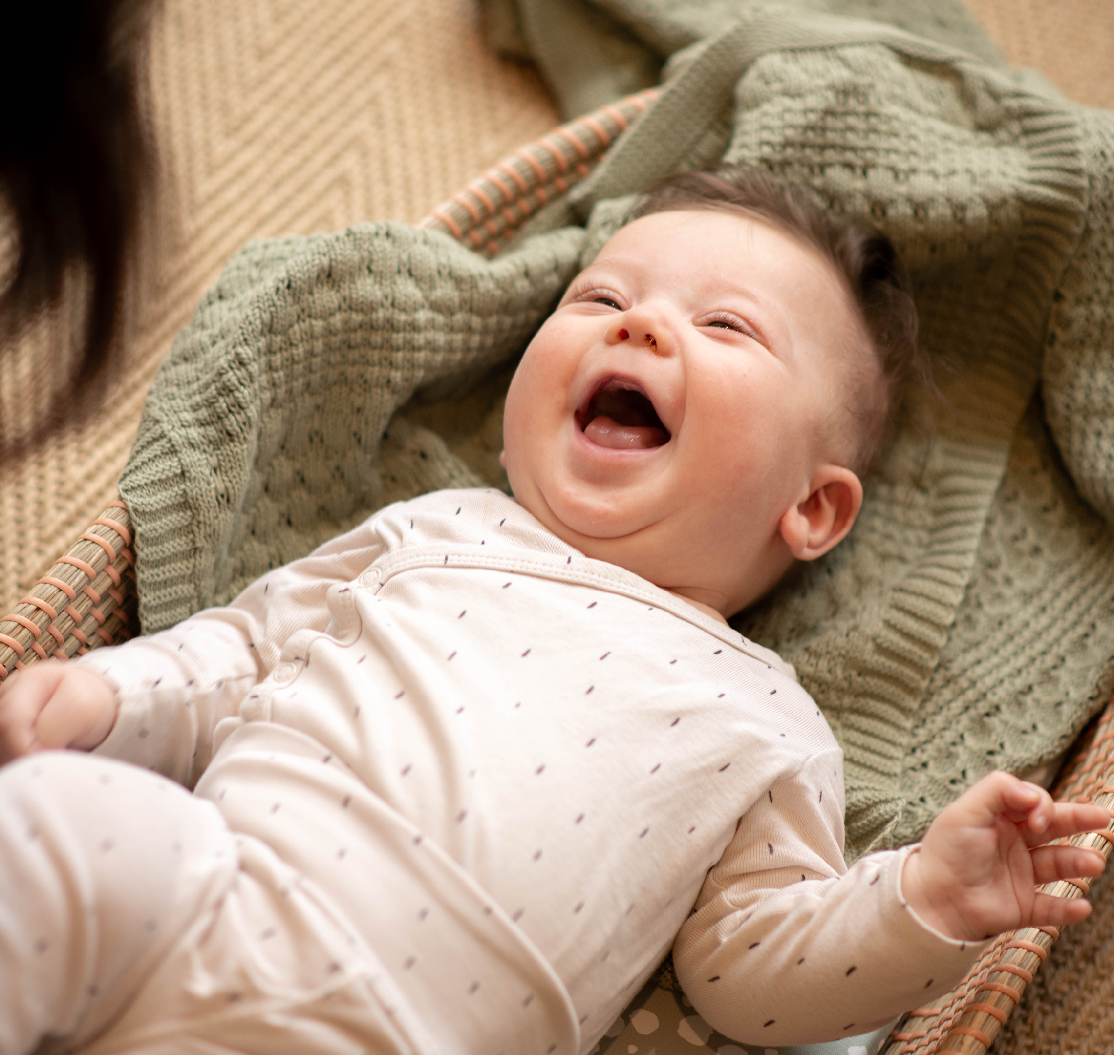 Smiling 6-week-old baby lying on a soft blanket, laughing up at a caregiver during playtime.