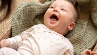 Smiling 6-week-old baby lying on a soft blanket, laughing up at a caregiver during playtime.