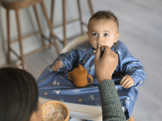 Little boy being fed porridge by mum