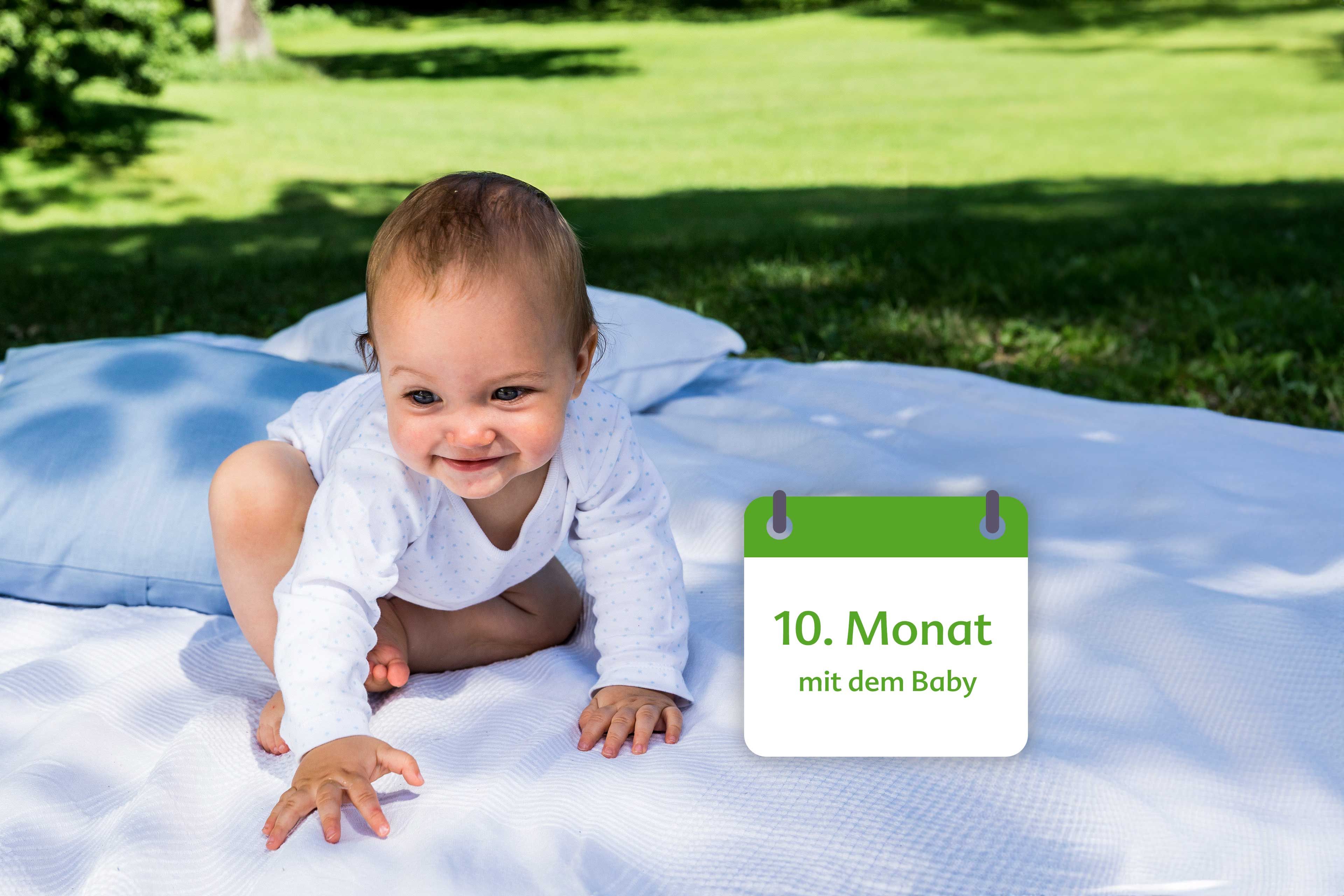 Ein Baby, vermutlich 10 Monate alt, spielt auf einer Decke im Freien.