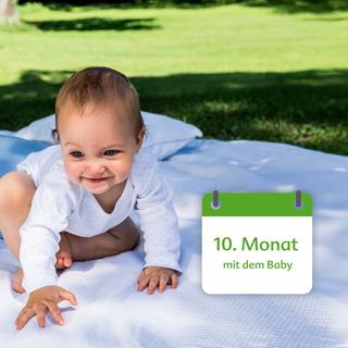Ein Baby, vermutlich 10 Monate alt, spielt auf einer Decke im Freien.