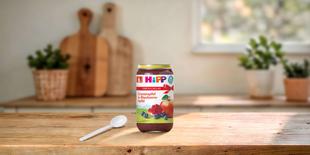 HiPP Bio Fruchtpüree Granatapfel in Blaubeere-Apfel im Vorteils-Glas auf Holztisch mit Löffel in heller Küche