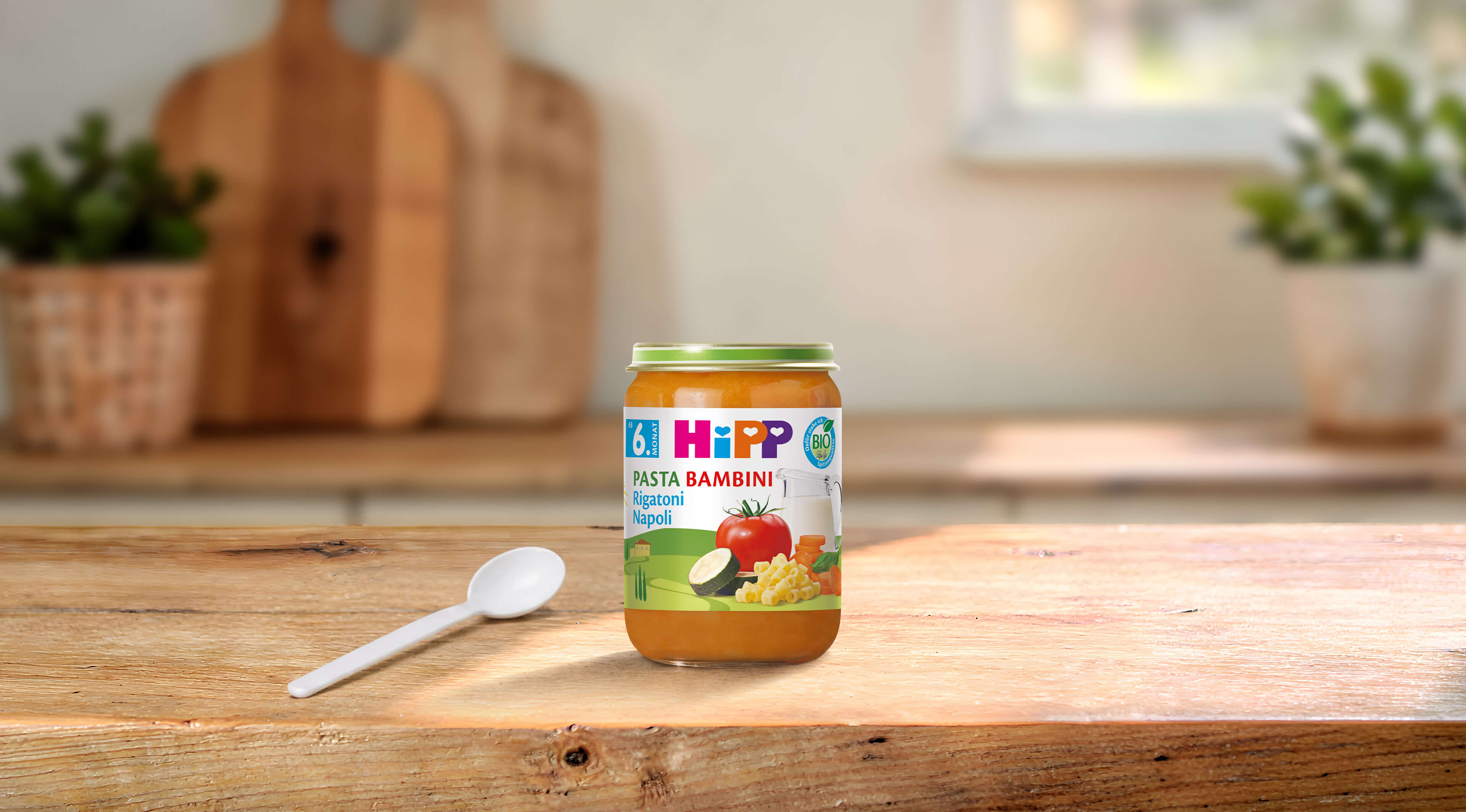 HiPP Pasta Bambini Rigatoni Napoli 190g Bio-Gläschen mit Löffel auf Holztisch in heller Küche
