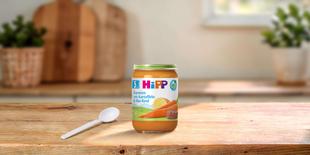 HiPP Bio-Gläschen Karotten mit Kartoffeln und Bio-Rind ab dem 5. Monat auf Holztisch mit Löffel in heller Küche