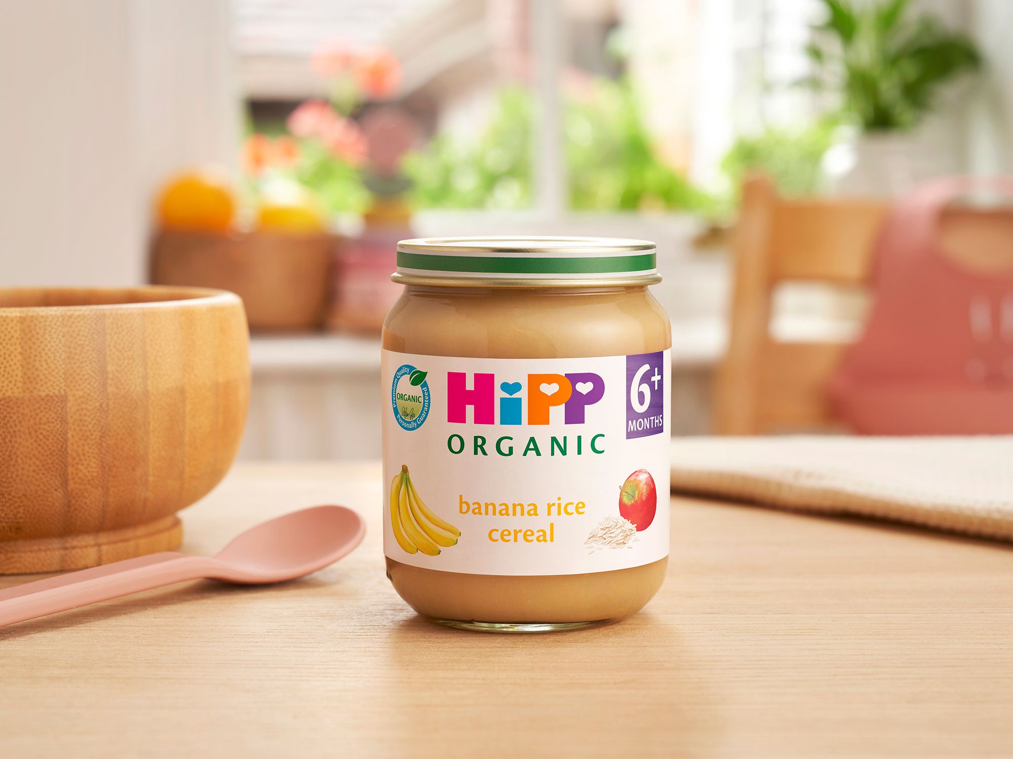 HiPP Organic Banana Rice Cereal jar on a dining table next to a bowl and spoon
