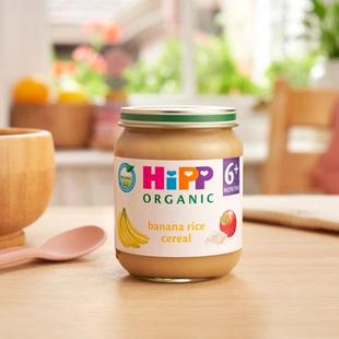 HiPP Organic Banana Rice Cereal jar on a dining table next to a bowl and spoon