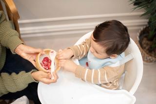Baby in high chair with bub reading out to mum holding a spoon and bowl filled with food