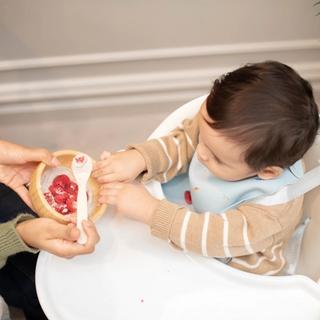 Baby in a highchair exploring a bowl of fruit with a parent, showing early fussy eating and mealtime learning