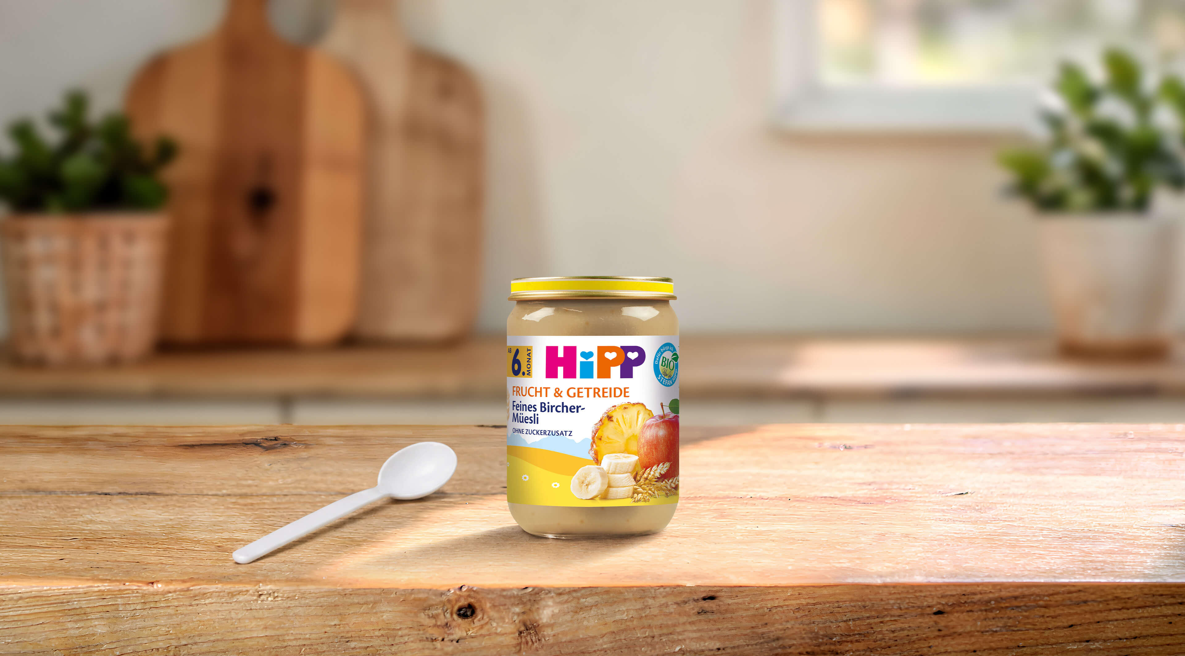 HiPP Frucht & Getreide Feines Bircher-Müesli Bio-Babygläschen auf Holztisch mit Löffel in heller Küche
